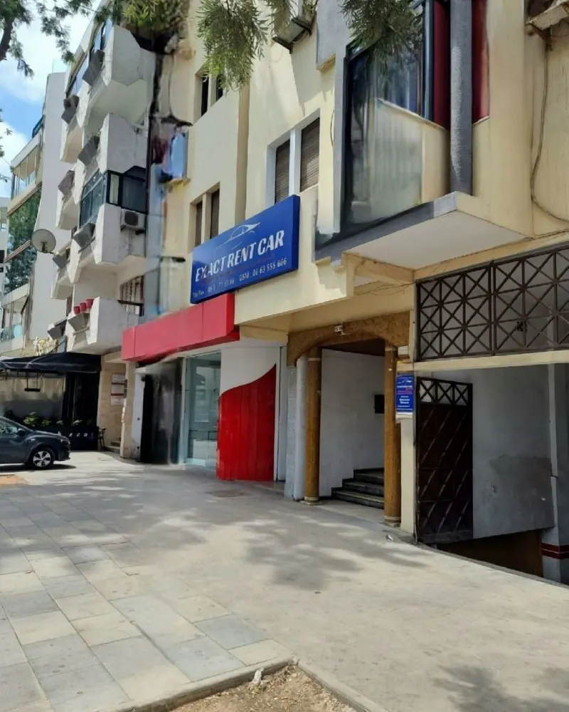 L’immeuble crème du 16 avenue Fal Ould Oumeir, avec l’enseigne bleue EXACT RENT CAR au-dessus d’un auvent rouge